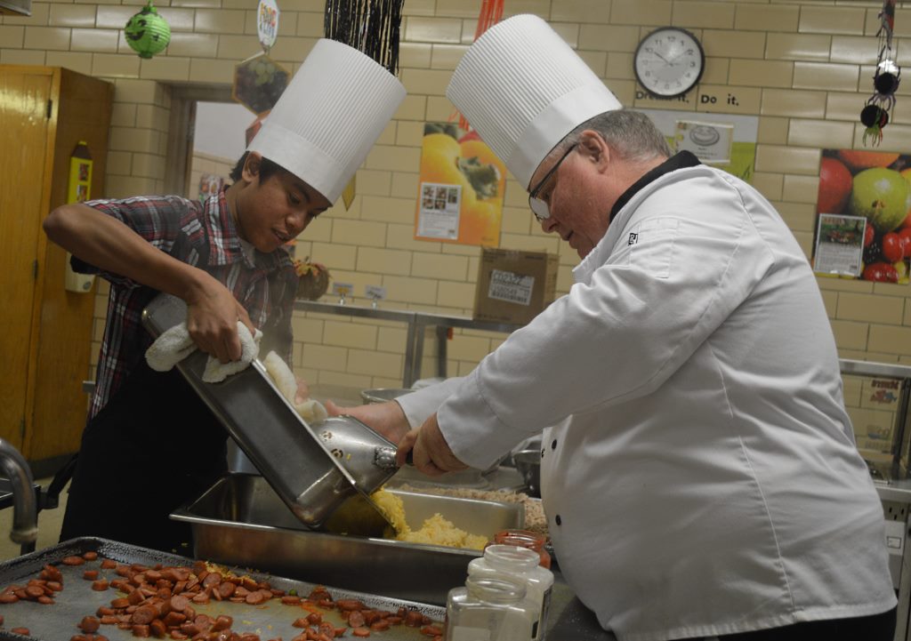 MLHS SENIOR LOUIS Louangthilath holds the pan as Chef Brian scoops out the hot rice, set to mixed with the remaining ingredients for the paella. Saffron, the spice that also turns the rice a wonderful golden color is an essential part of the dish.
