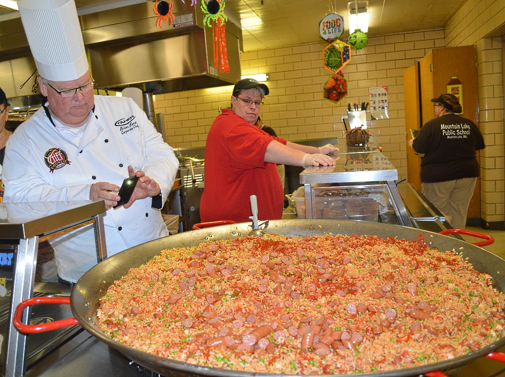 THE COMPLETED DISH is so tempting that Chef Brian snaps a quick photo to share on Facebook. Checking out the large plateful of paella is Carol Kipfer, right, of the kitchen staff.