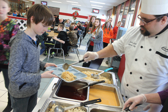 Leader Photo by Lee Pulaski Josh Good, right, a regional chef with Taher Inc., pours some curry lime coconut sauce on Thai noodles for Carson Cummings, a sixth-grade student at Shawano Community Middle School, Wednesday. Taher’s roving chef program gives students a chance to try different ethnic meals they wouldn’t ordinarily get to enjoy in the regular school lunch program.