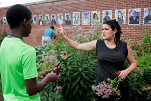 Rebecca Lemos-Otero (right), co-founder and co-executive director of City Blossoms, helps Erwin Tcheliebou, 15, pick flowers to sell at the farmers market. Behind her is a wall featuring the painted portraits of Eastern Senior High students who have worked in the garden. Lydia Thompson/NPR